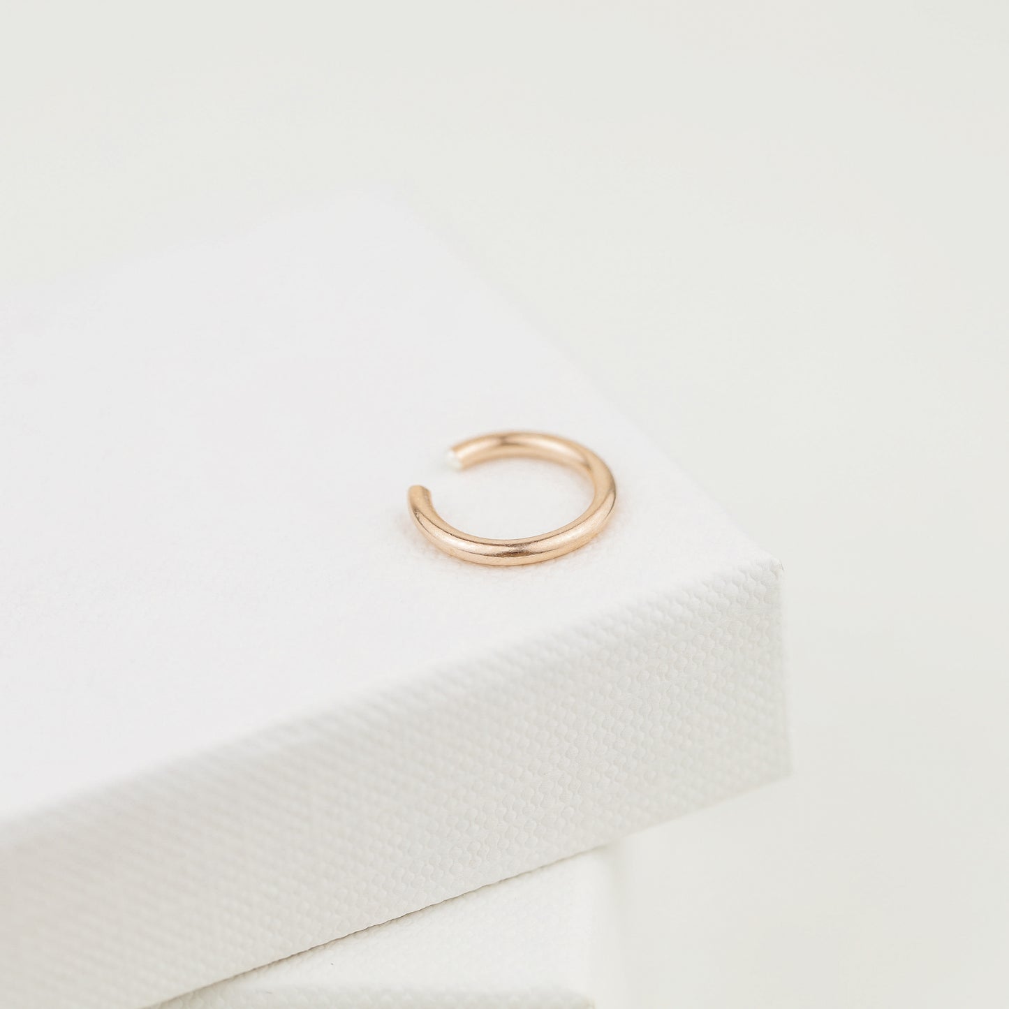Thick smooth no-piercing ear cuff shown worn on different areas of the ear, including lobe, conch, cartilage and upper helix, with a rounded wrap design available in sterling silver, 18k yellow gold plated sterling silver, 18k rose gold plated sterling silver and black aluminum.