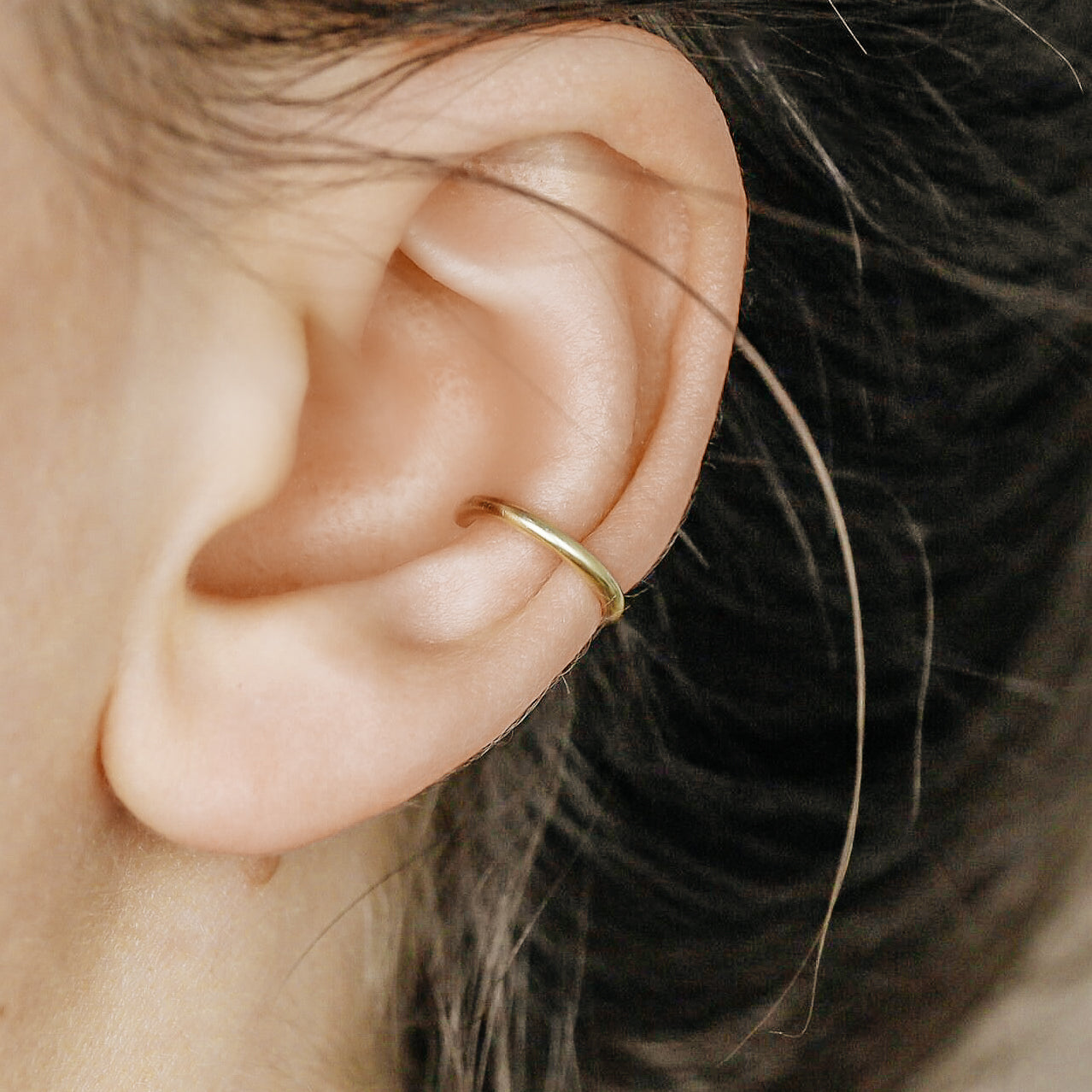 Thick smooth no-piercing ear cuff shown worn on different areas of the ear, including lobe, conch, cartilage and upper helix, with a rounded wrap design available in sterling silver, 18k yellow gold plated sterling silver, 18k rose gold plated sterling silver and black aluminum.