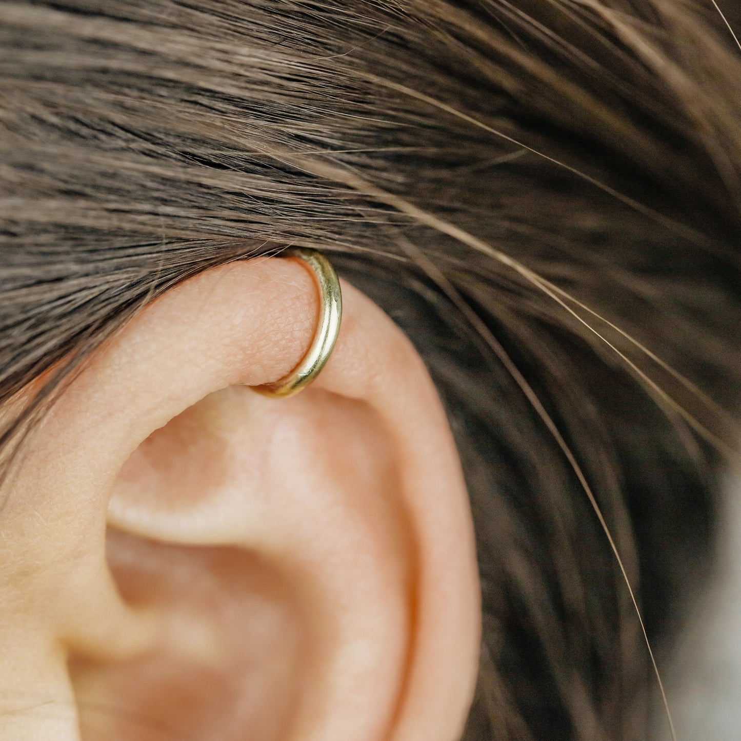 Thick smooth no-piercing ear cuff shown worn on different areas of the ear, including lobe, conch, cartilage and upper helix, with a rounded wrap design available in sterling silver, 18k yellow gold plated sterling silver, 18k rose gold plated sterling silver and black aluminum.