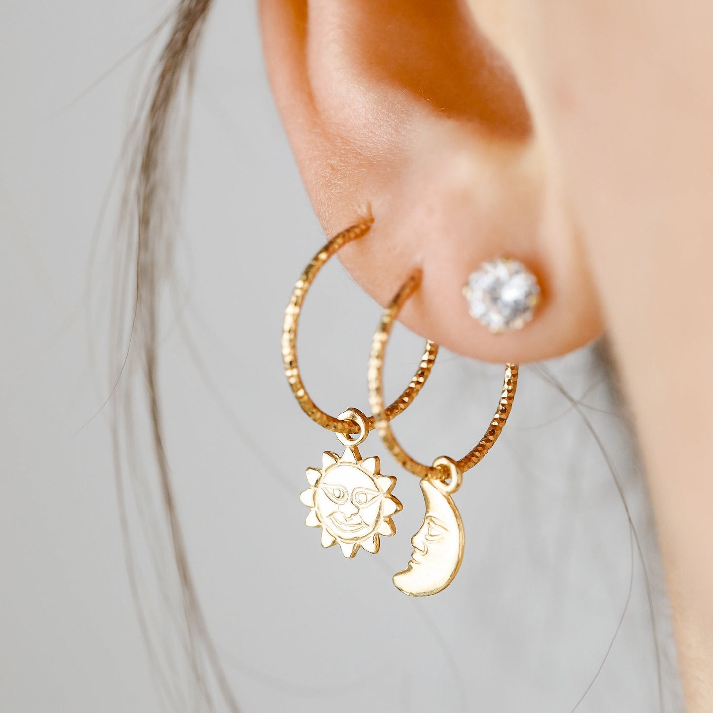 Single 18k yellow gold endless hoop earring featuring a diamond-cut textured finish and a smiling celestial sun charm pendant, shown in a cartilage helix piercing.