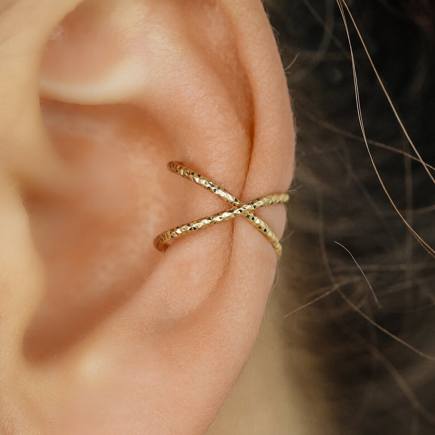 Diamond cut gold criss cross ear cuff worn on the upper ear, designed as a no piercing conch ear cuff with sparkling textured finish.