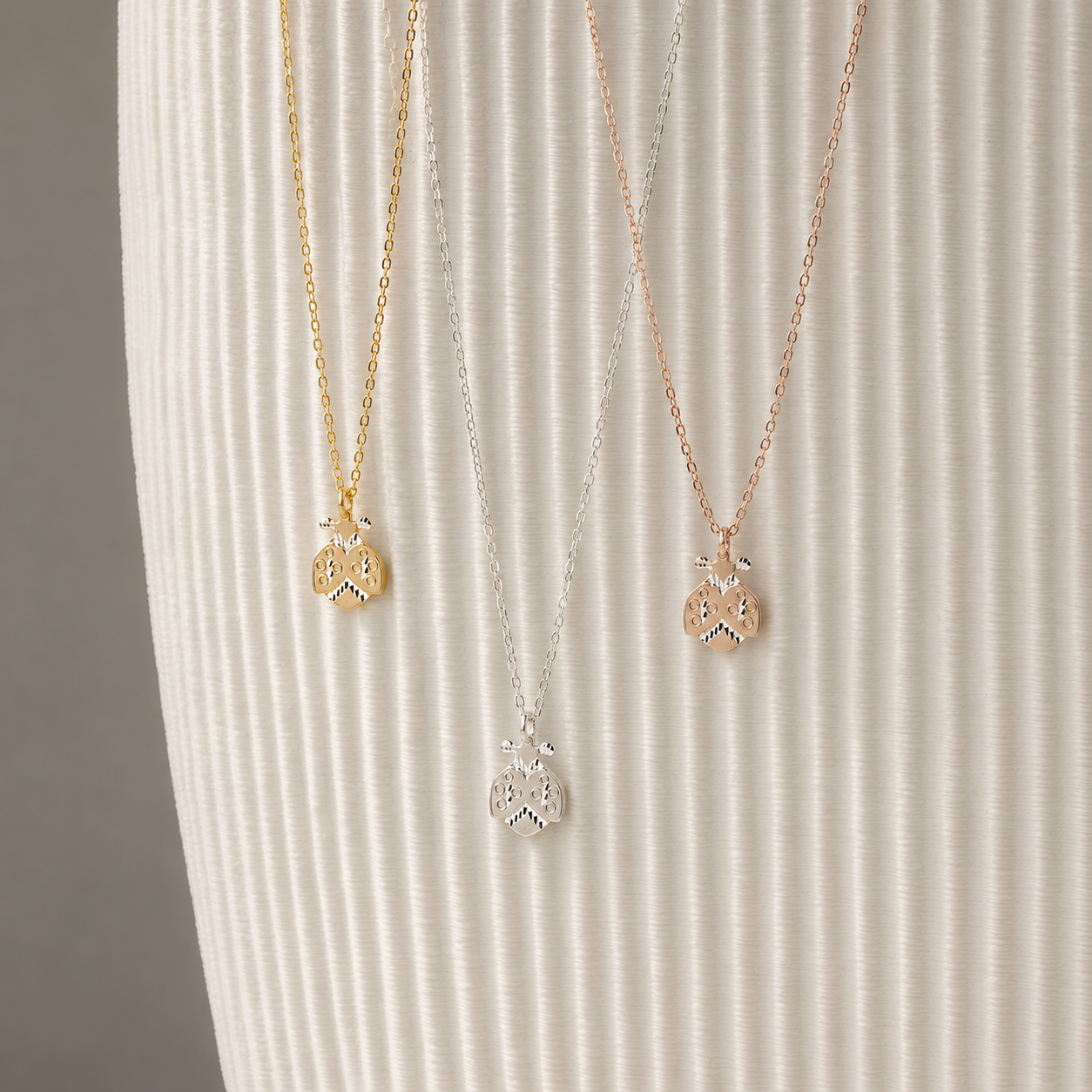 Ladybug necklaces displayed in silver gold and rose gold finishes on neutral ribbed background