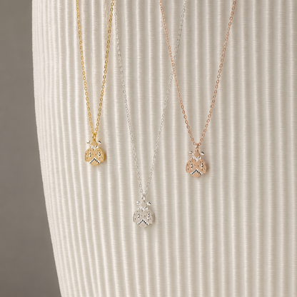 Ladybug necklaces displayed in silver gold and rose gold finishes on neutral ribbed background
