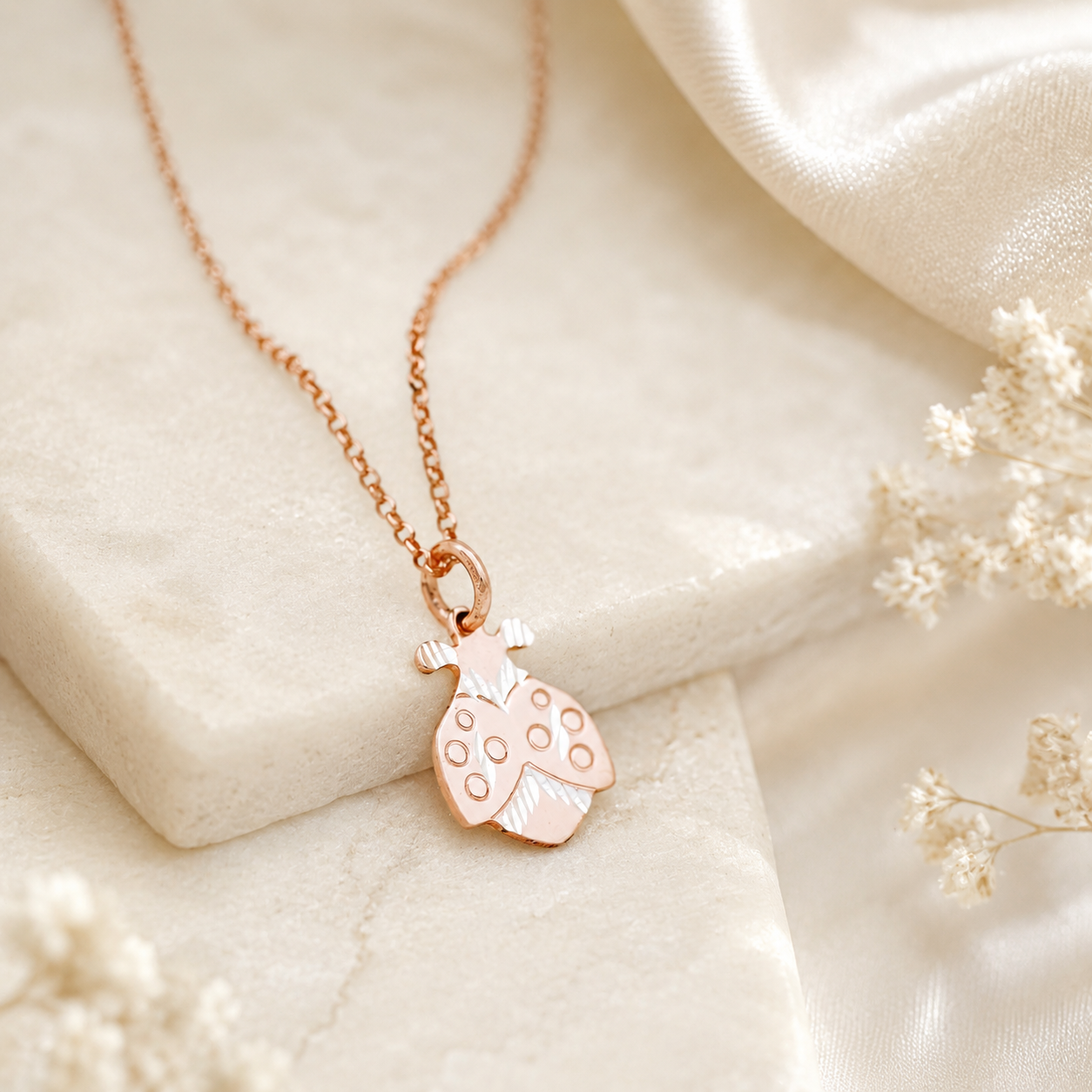 Rose gold ladybug pendant necklace displayed on neutral stone with delicate dried flowers