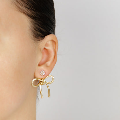 Gold medium bow ear jacket worn behind the earlobe with a small floral stud, showing how the handmade hammered bow sits under the ear.