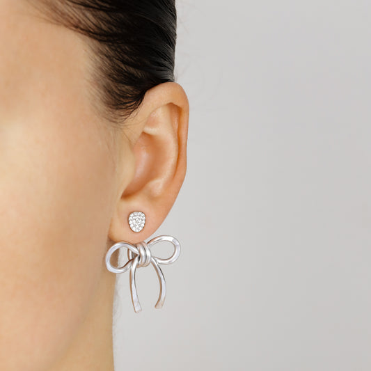 Silver medium bow ear jacket worn behind the earlobe with a sparkling stud, highlighting the lightweight hammered aluminum design.