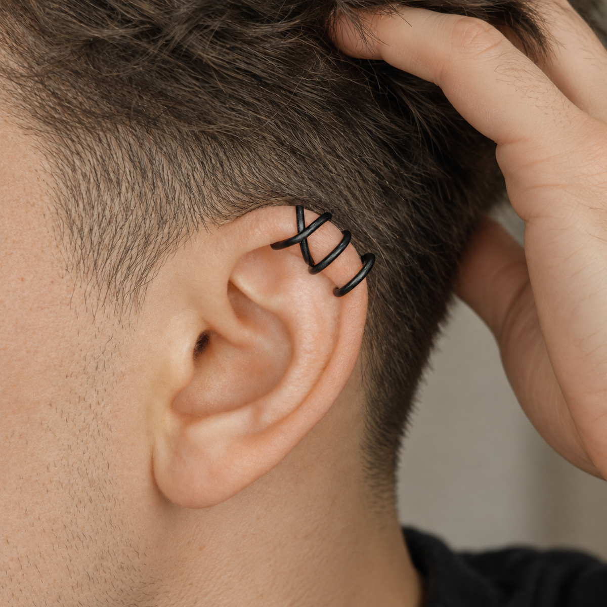 Man wearing a black Criss-Cross helix ear cuff on the upper ear, styled with short hair for a clean contemporary masculine look.