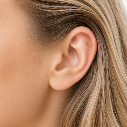 Close up of minimal gold bar screw back earring worn in upper helix piercing on blonde model with natural lighting and soft wavy hair