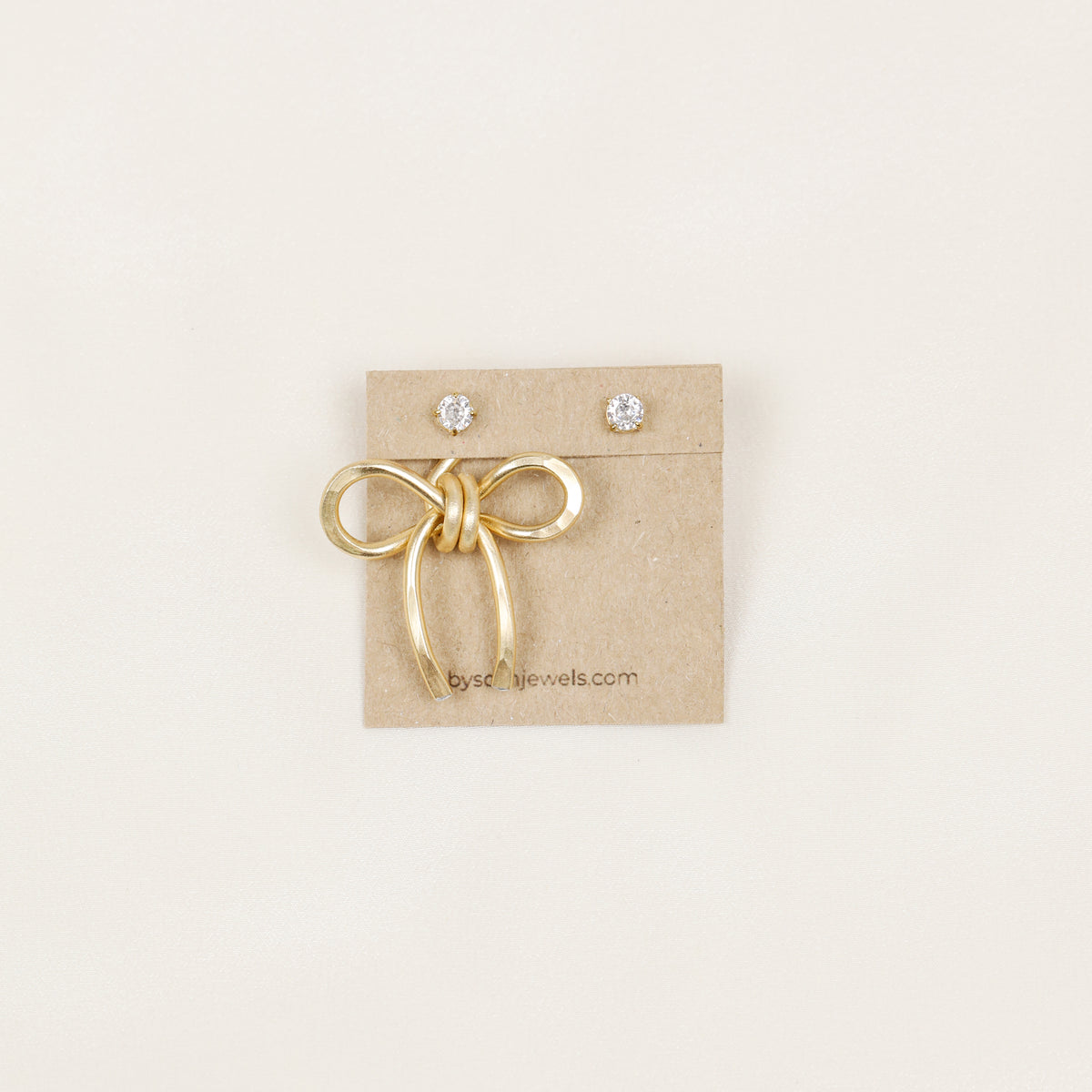 Single gold medium bow ear jacket displayed on a jewelry card with crystal stud earrings, showing the one ear jacket option.