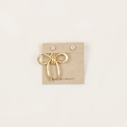 Single gold medium bow ear jacket displayed on a jewelry card with crystal stud earrings, showing the one ear jacket option.