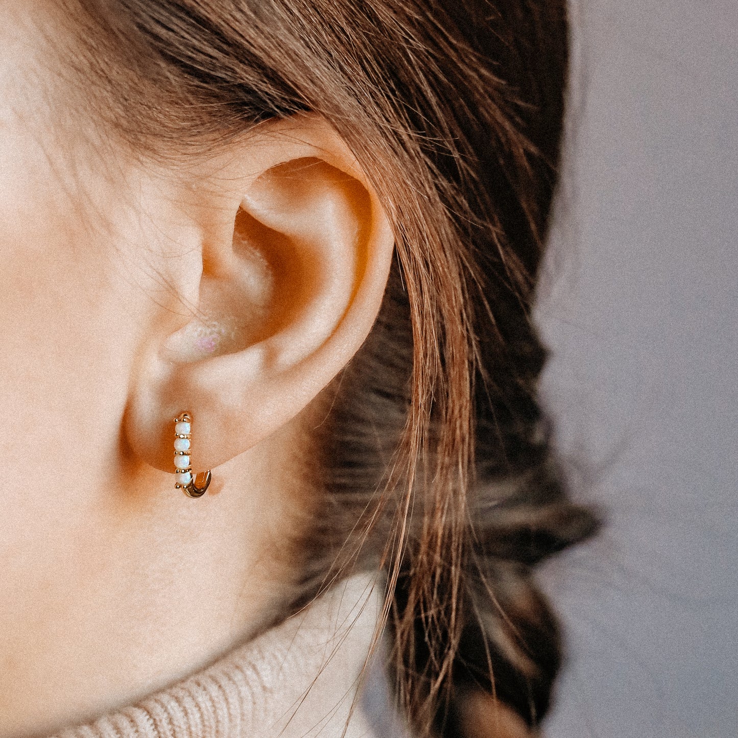 Gold opal huggie earrings worn on the lobe with a small rectangular hoop shape