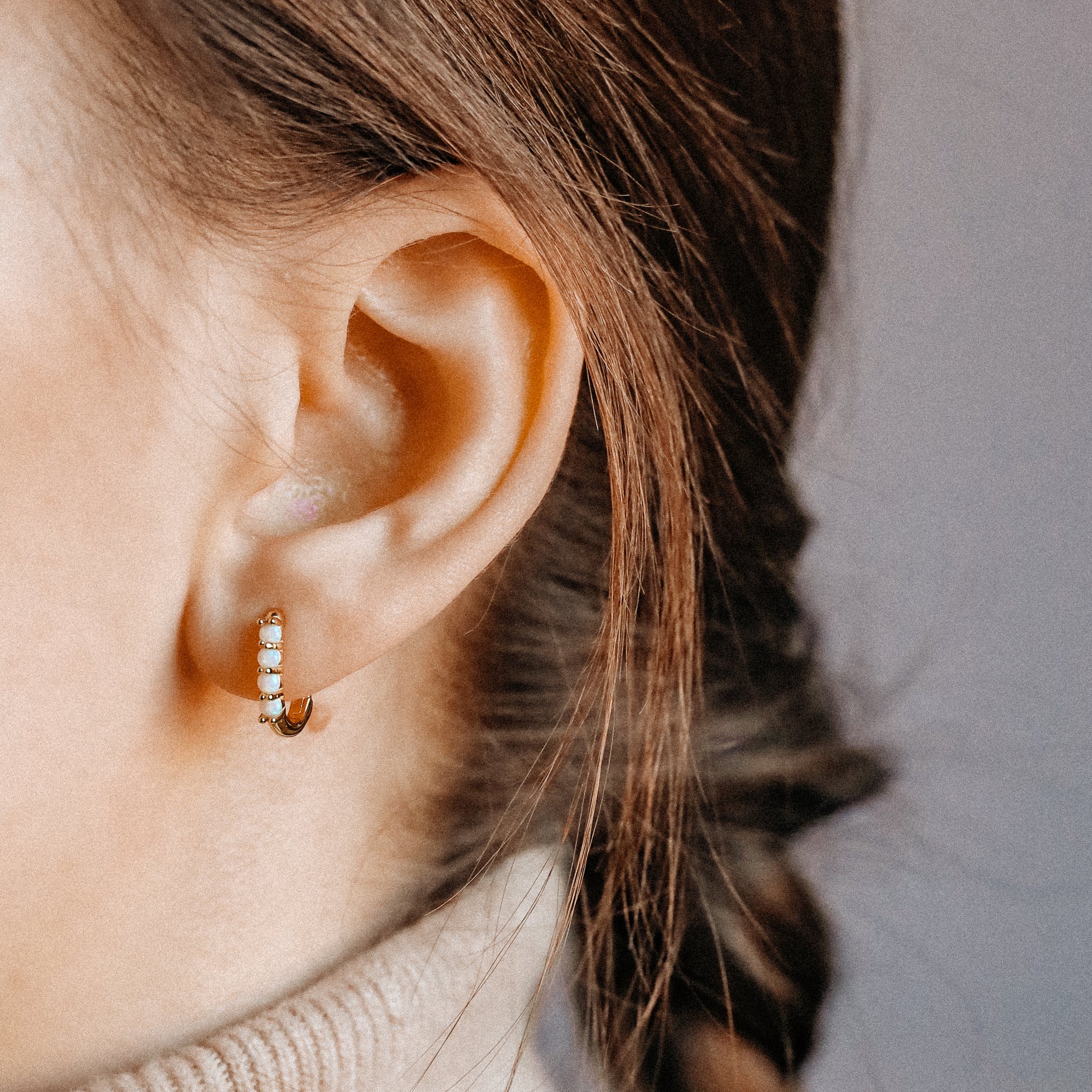 Gold opal huggie earrings worn on the lobe with a small rectangular hoop shape