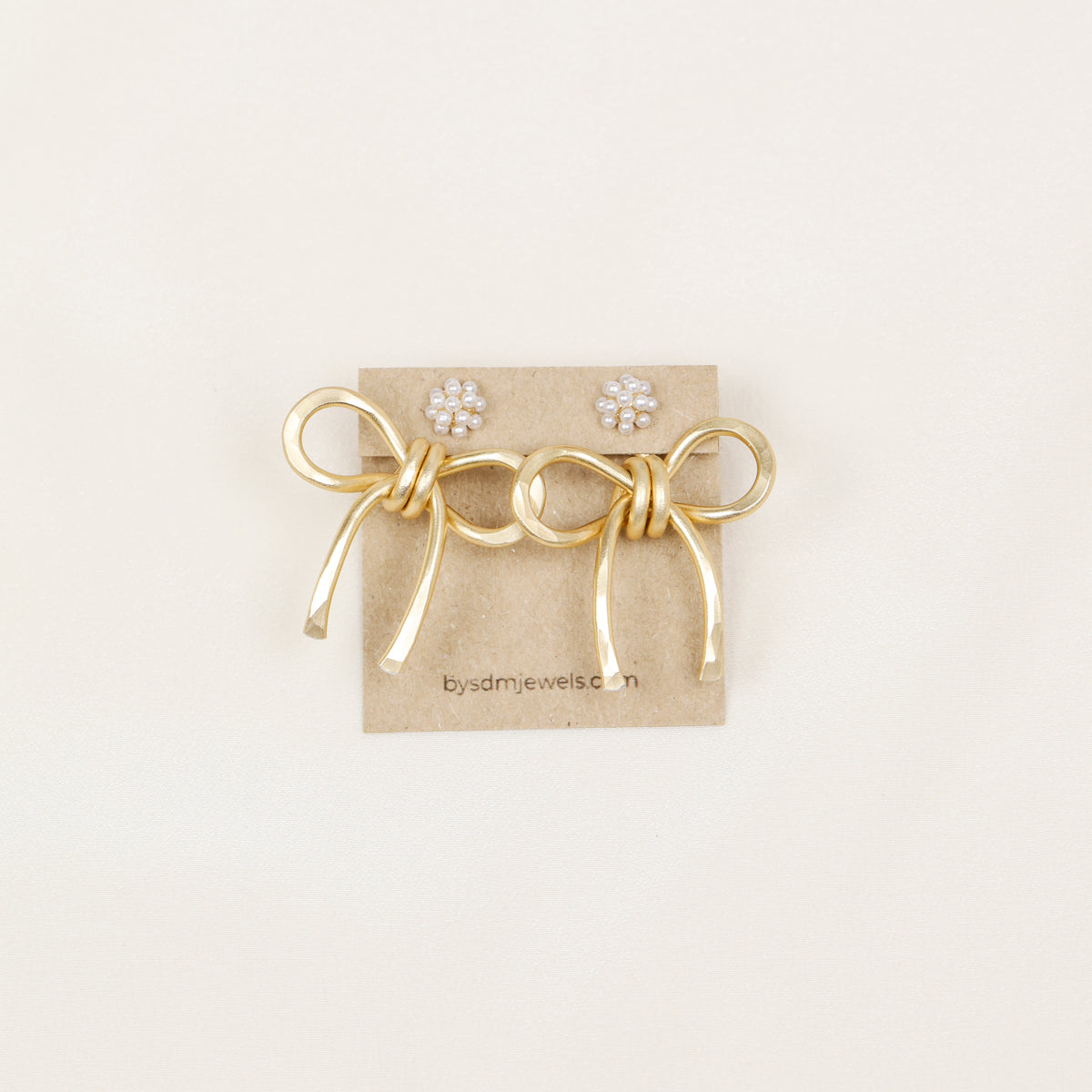 Pair of gold medium bow ear jackets displayed on a jewelry card with pearl-style stud earrings, highlighting the medium bow shape and hammered finish.