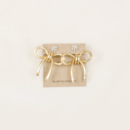 Pair of gold medium bow ear jackets displayed on a jewelry card with pearl-style stud earrings, highlighting the medium bow shape and hammered finish.