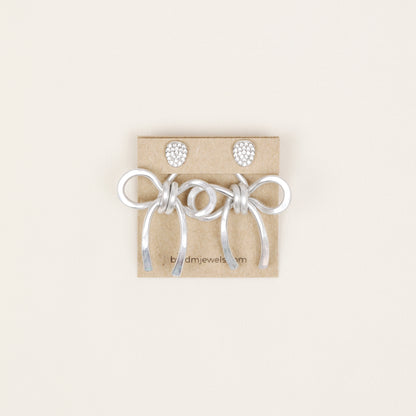 Pair of silver medium bow ear jackets displayed on a jewelry card with stud earrings, showing the full matching pair option.