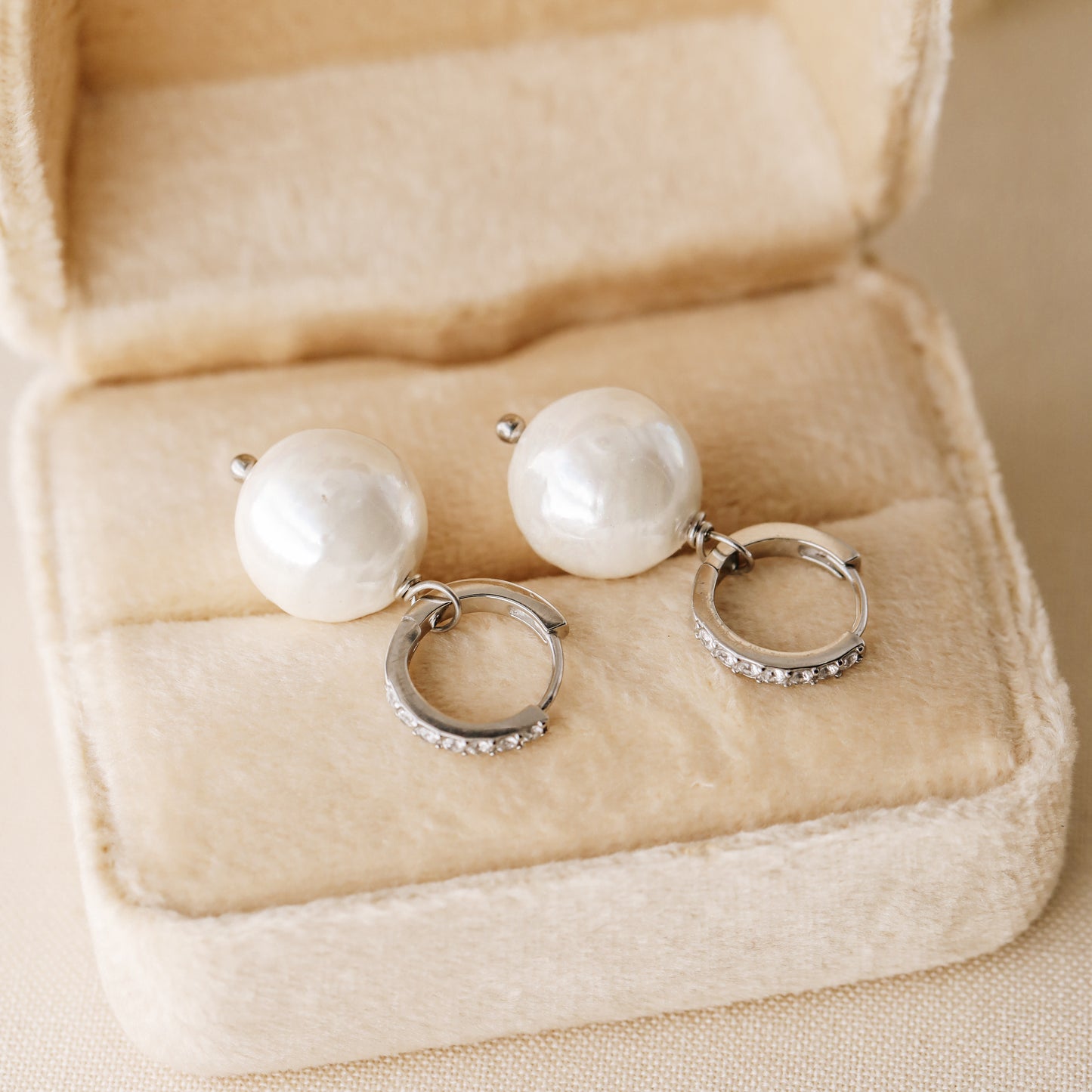Pearl drop hoop earrings displayed in a soft jewelry box with round ceramic pearls and silver hoops
