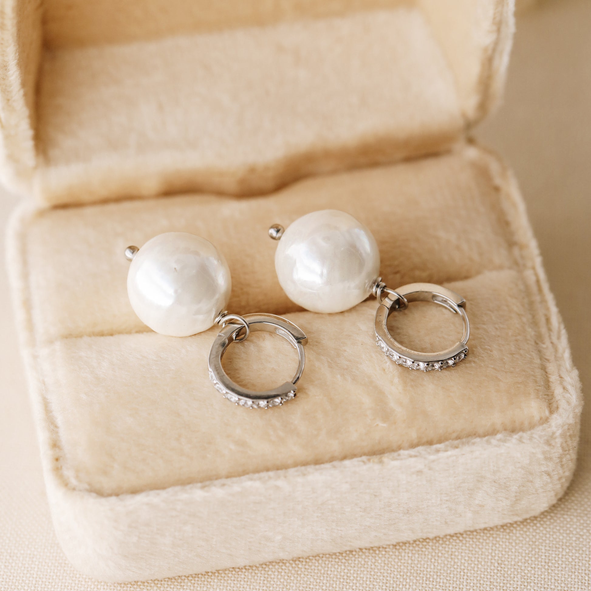 Pearl drop hoop earrings displayed in a soft jewelry box with round ceramic pearls and silver hoops