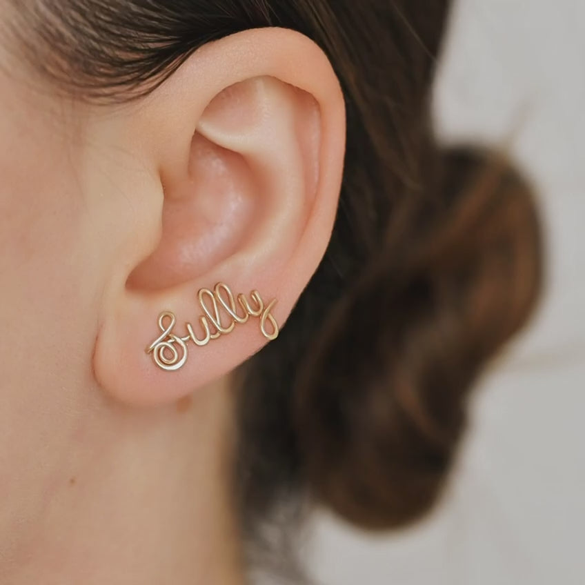 Handmade personalized name ear climber worn across the lobe through one standard piercing, featuring a custom flowing wire script design made with the chosen name or word up to 10 characters, available as a single left ear climber, single right ear climber or pair in solid 925 sterling silver, 14k gold filled and 14k rose gold filled.