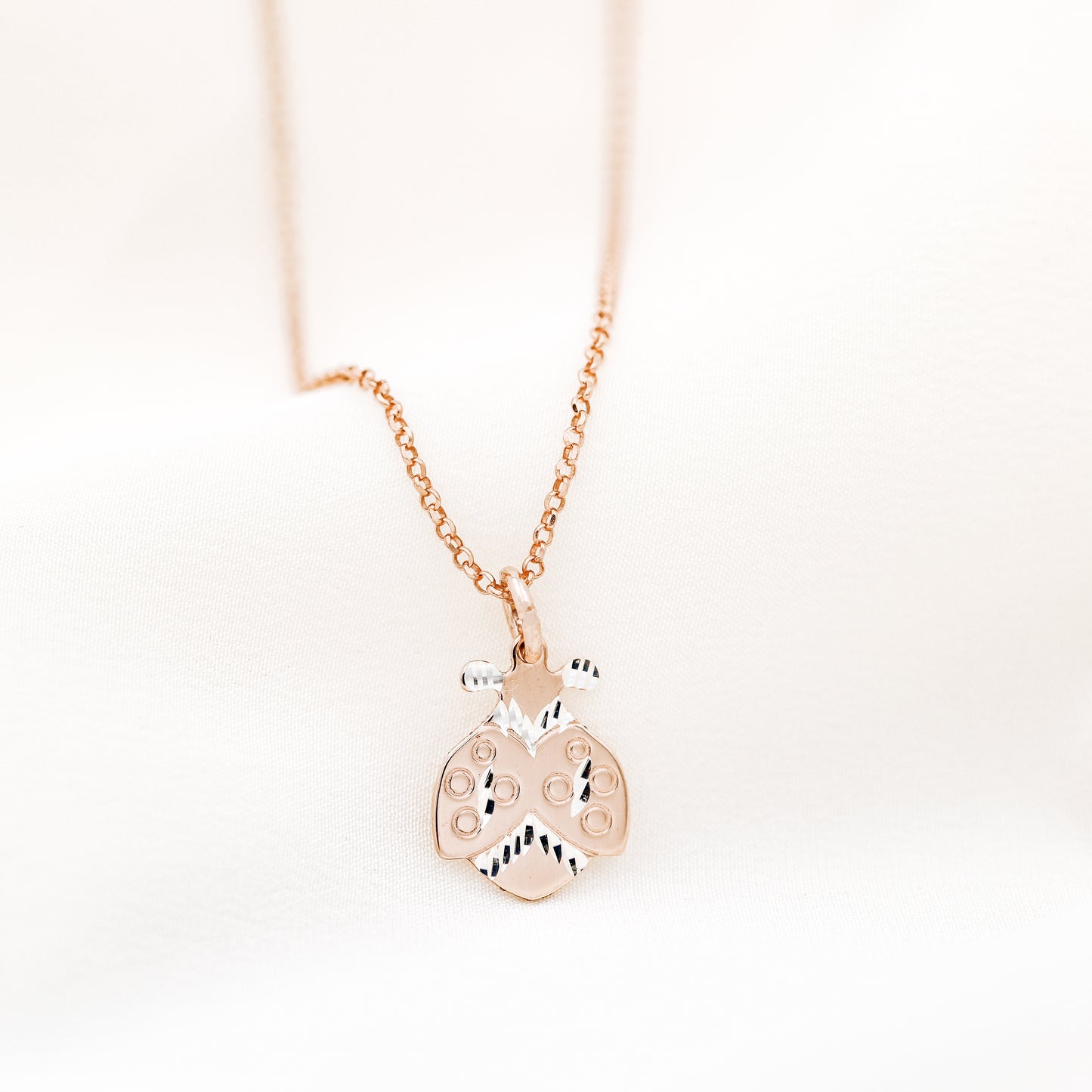 Rose gold ladybug necklace close up on soft white fabric background