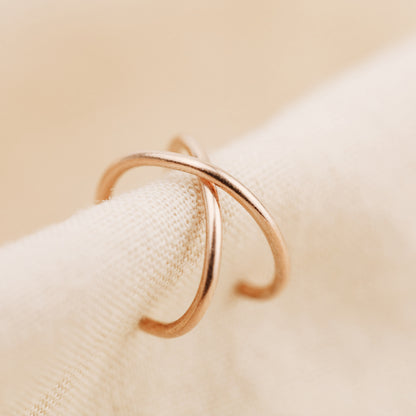 Rose gold smooth criss cross ear cuff displayed on soft beige fabric, featuring a minimal no piercing ear wrap design.