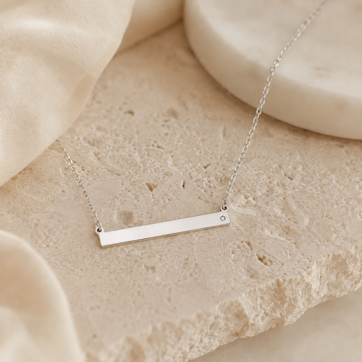 Sterling silver bar necklace photographed flat on round neutral stone surface