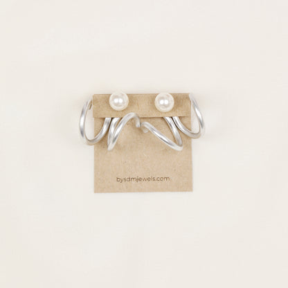 Pair of silver wavy double loop Ear Jackets displayed with pearl-style stud earrings, showing the matching pair configuration and flowing curved shape.