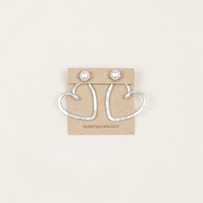 Pair of handmade silver aluminum Heart Ear Jackets displayed on a jewelry card with pearl-style stud earrings, showing the open hammered heart shape.