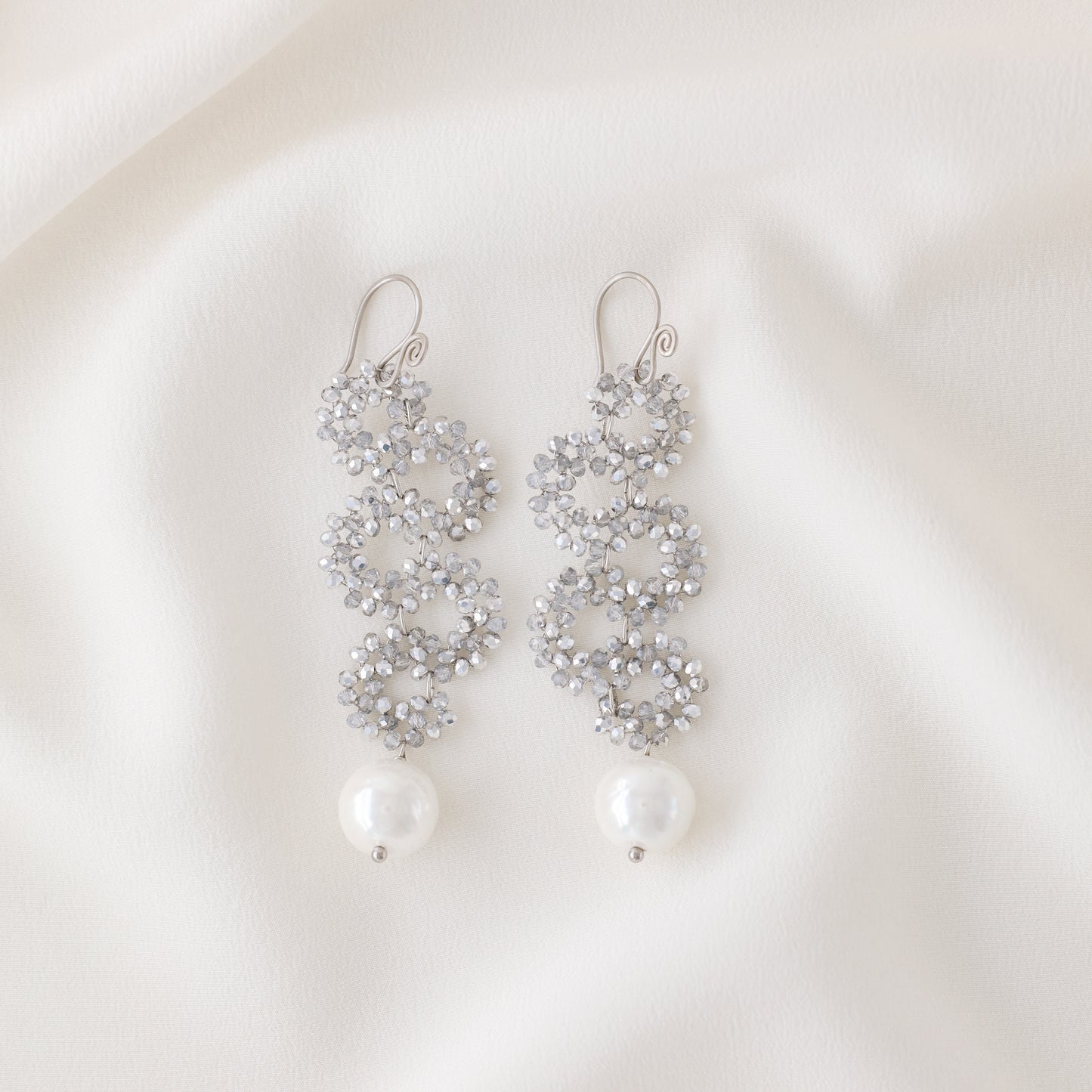 Silver iridescent snake-inspired earrings with crystal beaded circles and pearl drop on white fabric