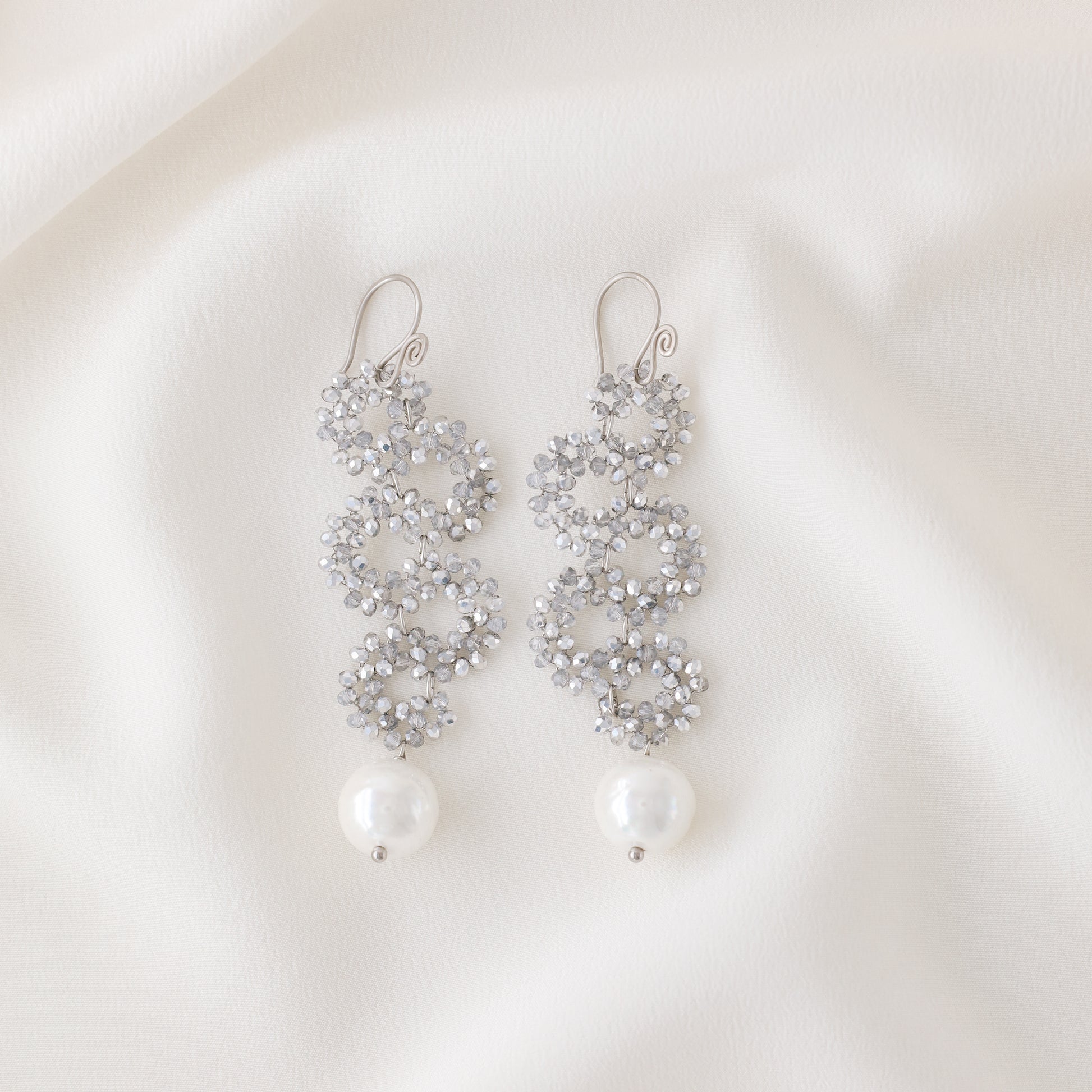 Silver iridescent snake-inspired earrings with crystal beaded circles and pearl drop on white fabric