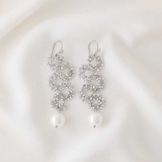 Silver iridescent snake-inspired earrings with crystal beaded circles and pearl drop on white fabric