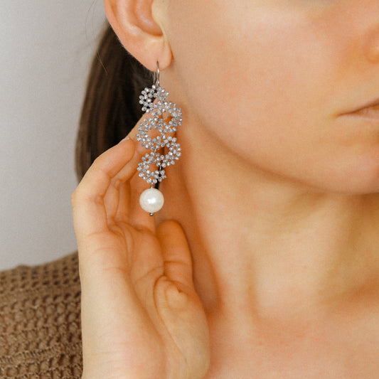 Silver iridescent snake earrings worn on ear with sparkling crystal beads and pearl drop