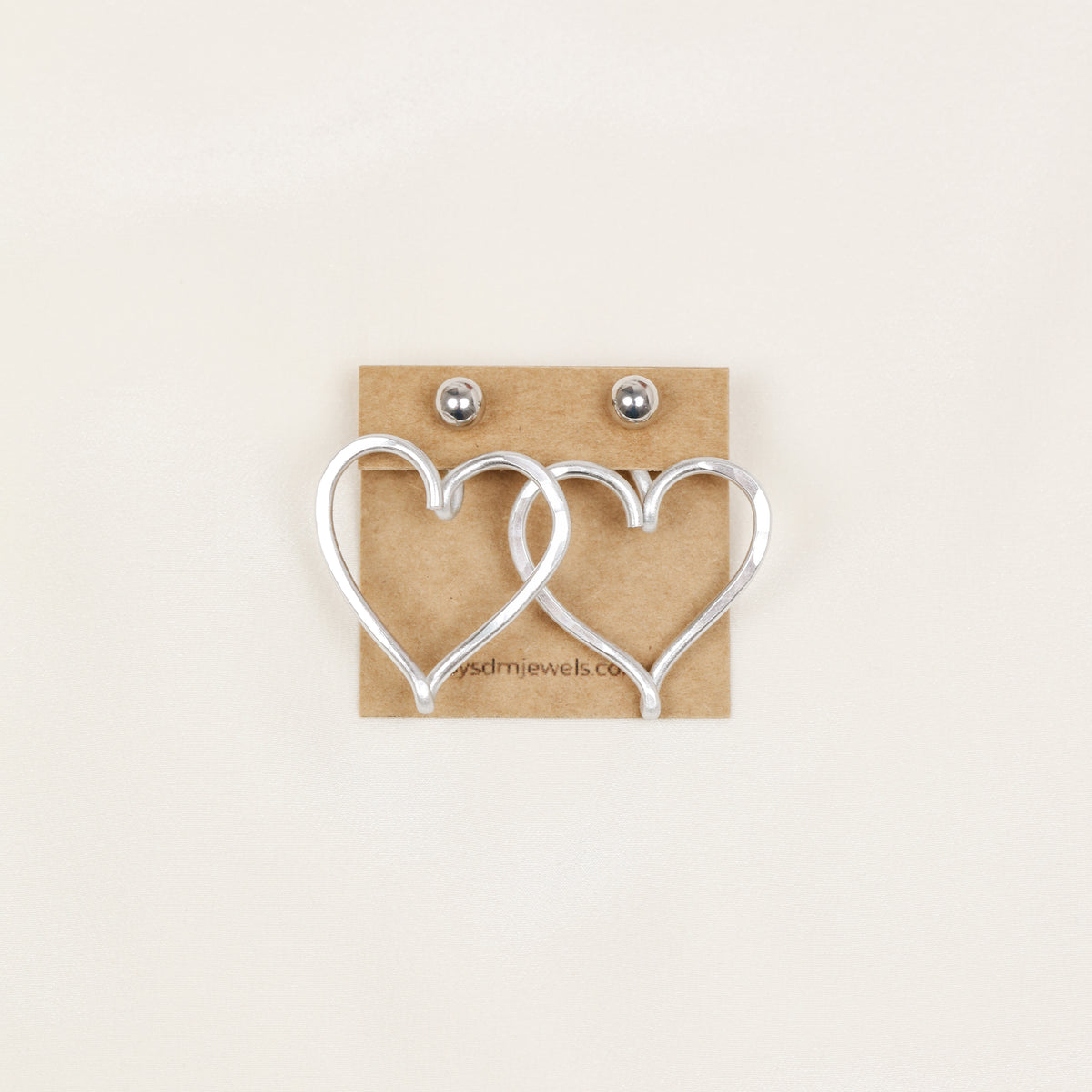 Pair of silver Large Heart Ear Jackets displayed on a jewelry card with silver ball stud earrings, showing the matching pair configuration and sculptural open heart shape.