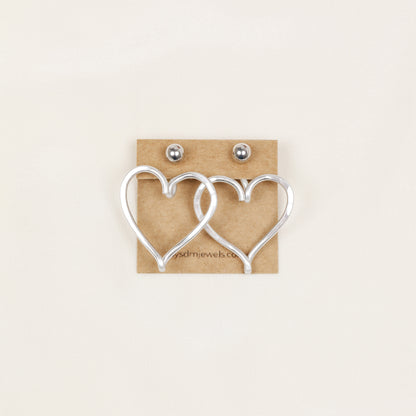 Pair of silver Large Heart Ear Jackets displayed on a jewelry card with silver ball stud earrings, showing the matching pair configuration and sculptural open heart shape.