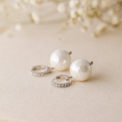 Silver pearl drop hoop earrings styled on neutral fabric with soft floral background