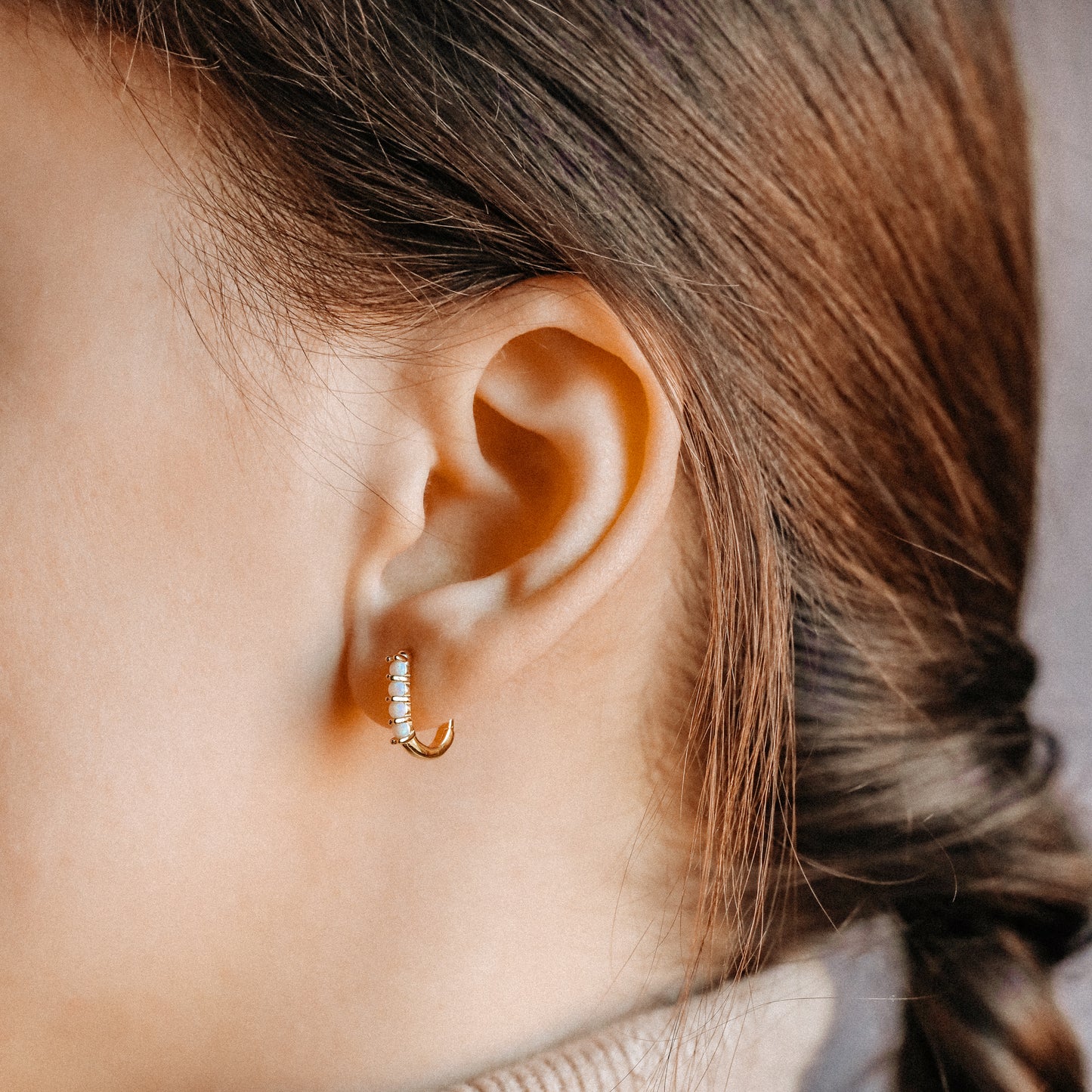 Small gold opal huggie hoop earrings worn for an everyday minimal look