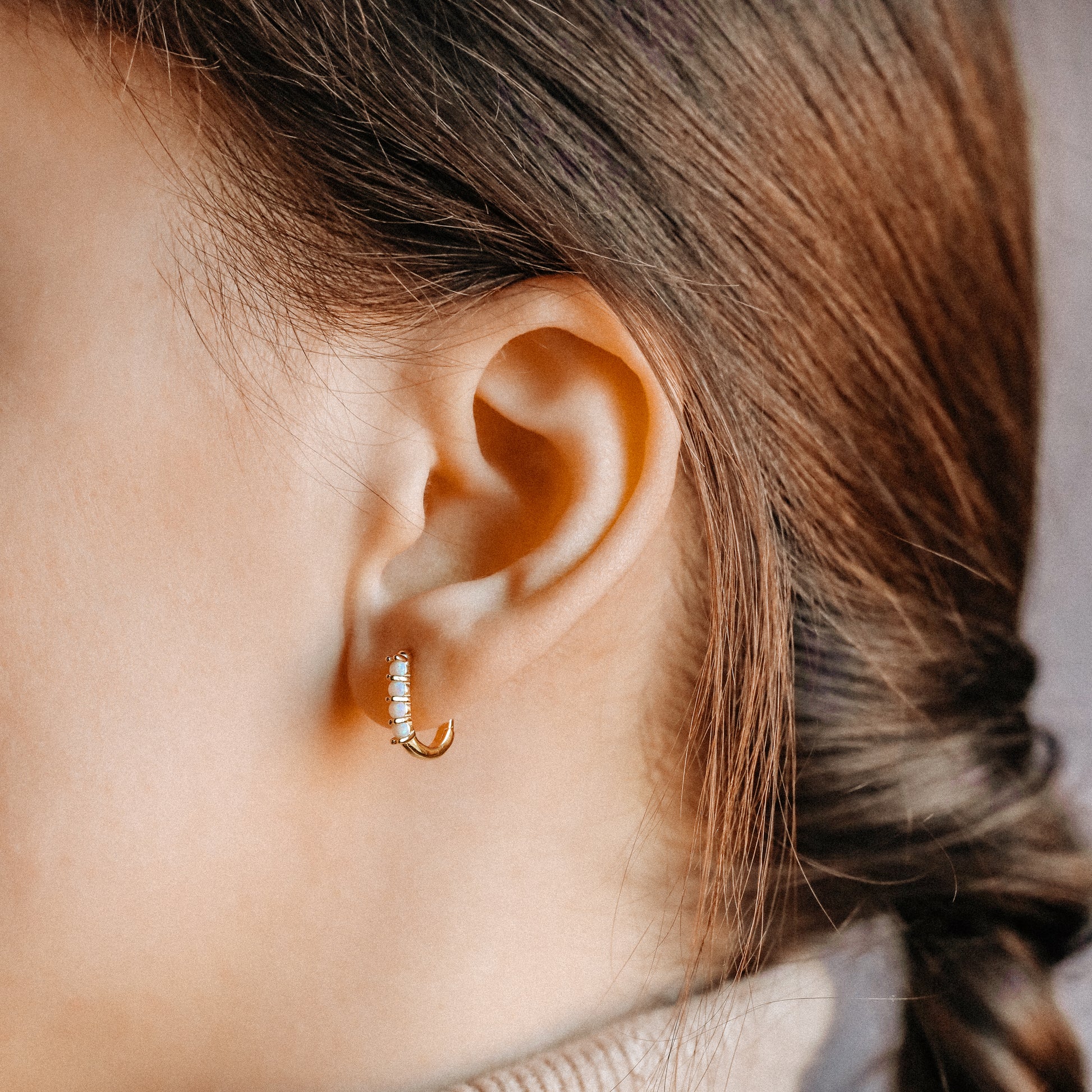 Small gold opal huggie hoop earrings worn for an everyday minimal look