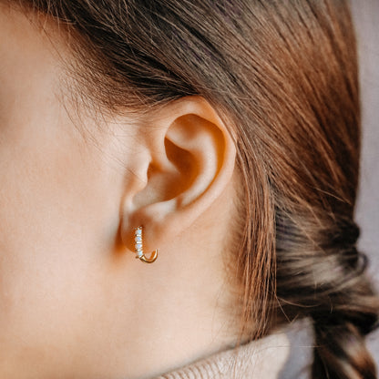 Small gold opal huggie hoop earrings worn for an everyday minimal look
