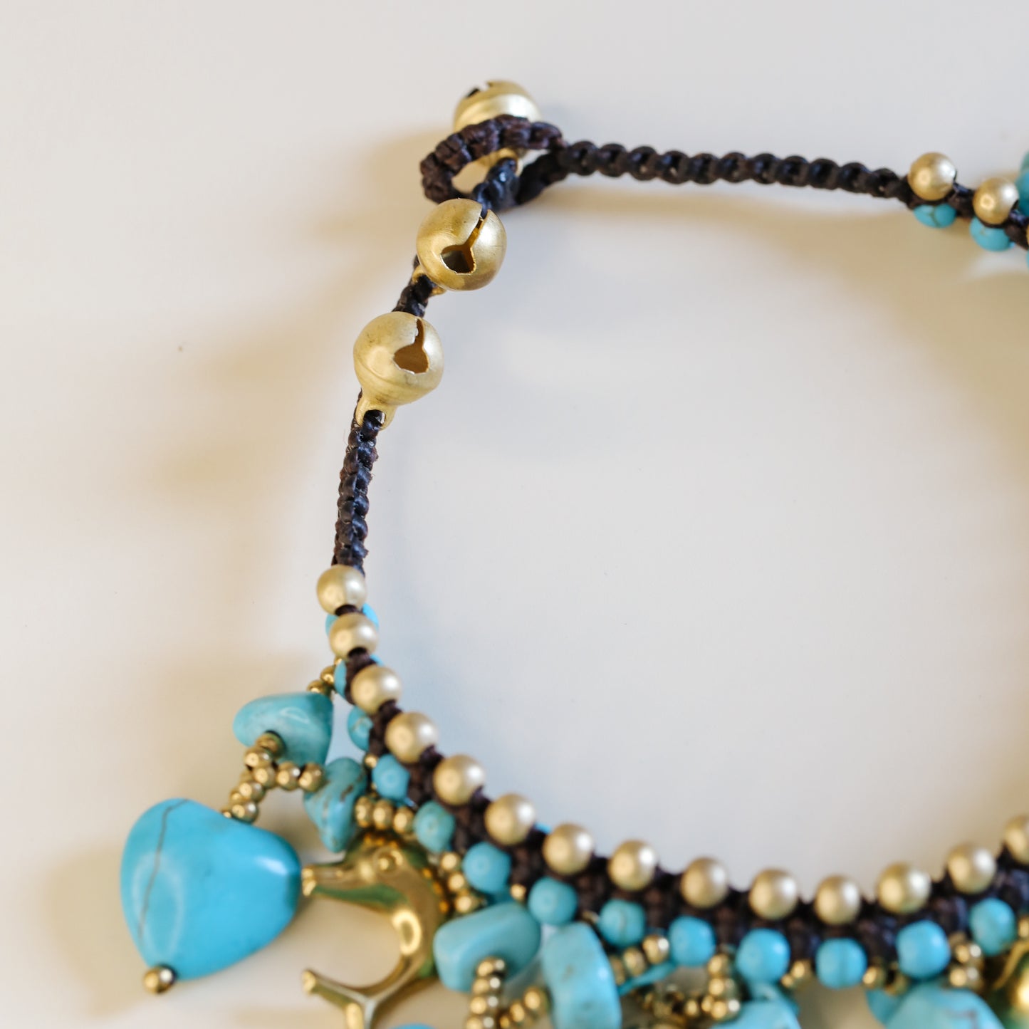 Close-up of the brown waxed cord and adjustable loop closure with small gold-tone bells on the turquoise anklet.