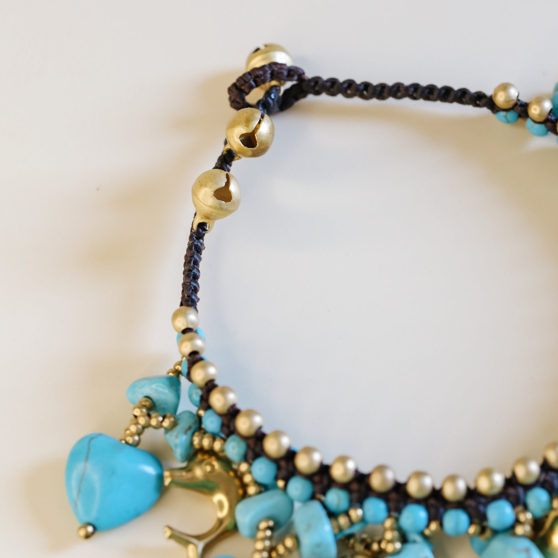 Close-up of the brown waxed cord and adjustable loop closure with small gold-tone bells on the turquoise anklet.