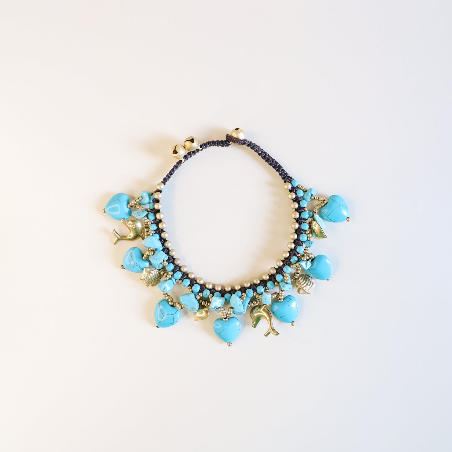 Close-up of adjustable turquoise anklet with brown cord, brass beads, heart charms, dolphins, fish and lucky bells.