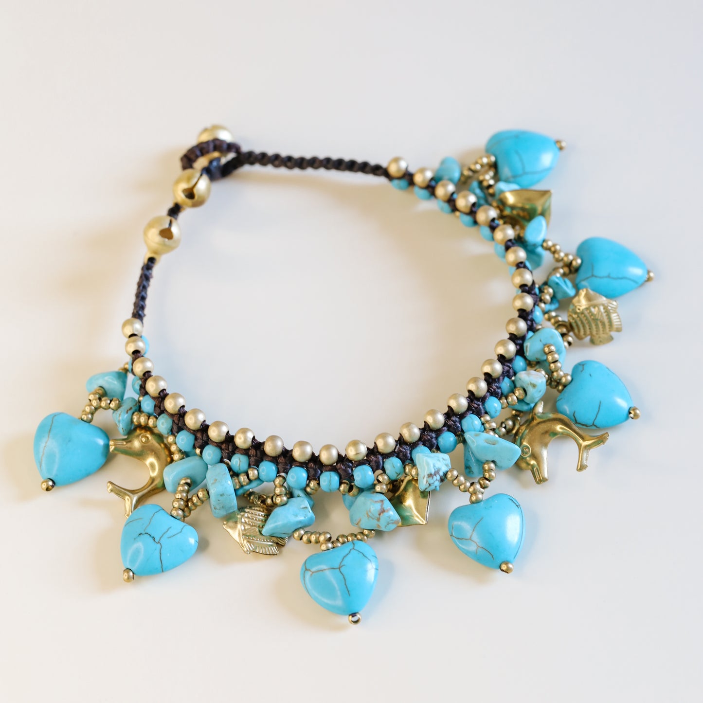 Detailed view of turquoise heart stones, small beads and antique gold-tone charms on a boho summer anklet.