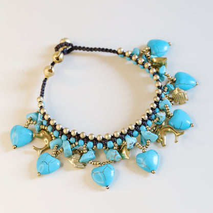 Detailed view of turquoise heart stones, small beads and antique gold-tone charms on a boho summer anklet.