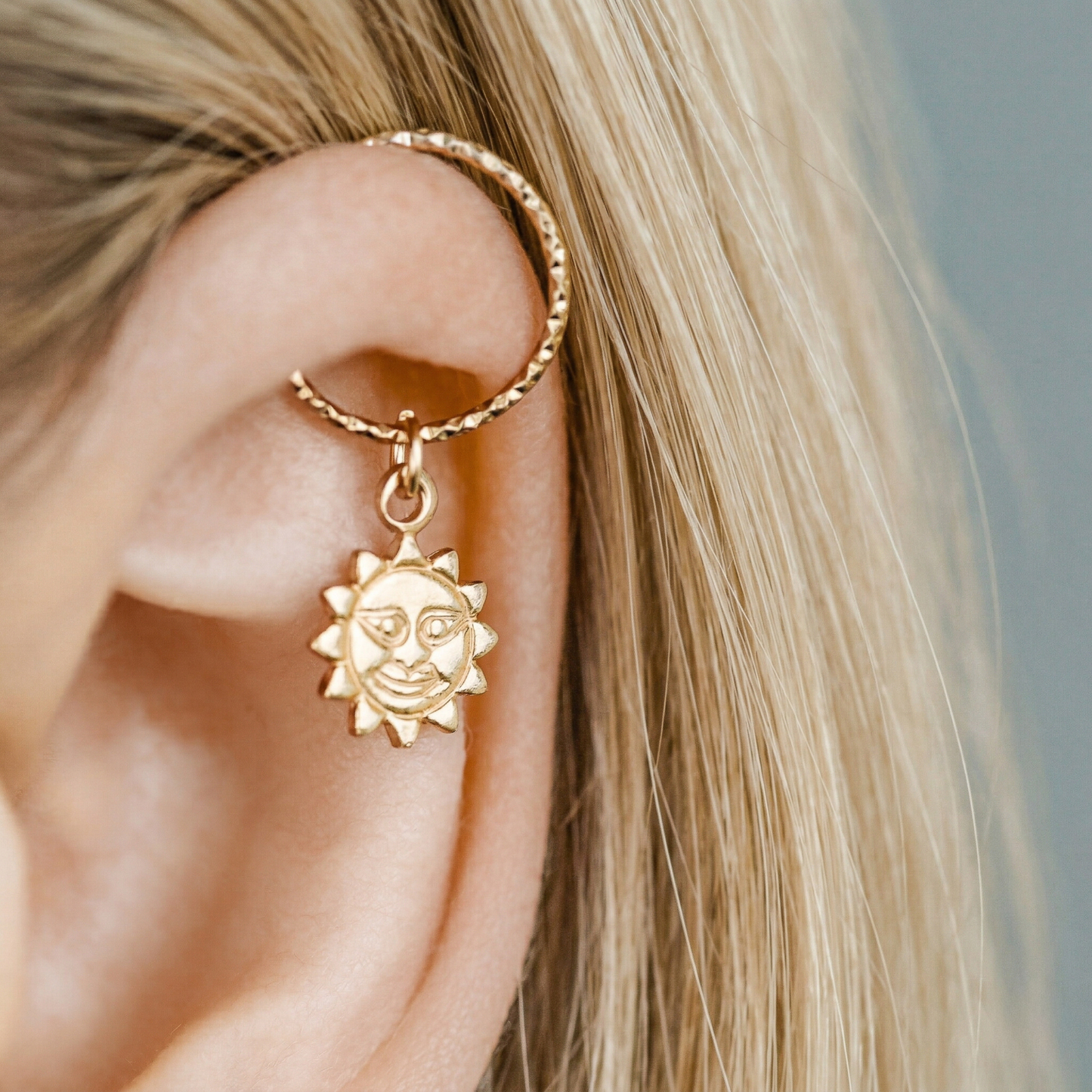 Single 18k yellow gold endless hoop earring featuring a diamond-cut textured finish and a smiling celestial sun charm pendant, shown in a cartilage helix piercing.
